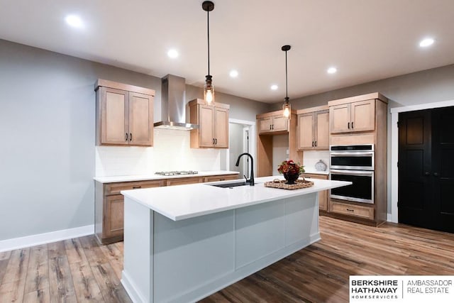 kitchen with sink, wall chimney exhaust hood, dark hardwood / wood-style floors, double oven, and an island with sink