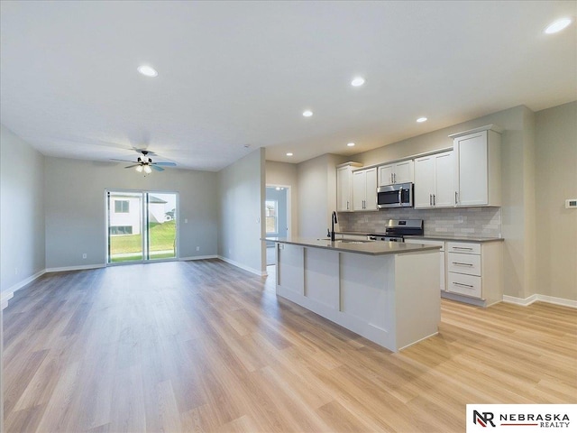 kitchen with ceiling fan, sink, stainless steel appliances, a kitchen island with sink, and light wood-type flooring