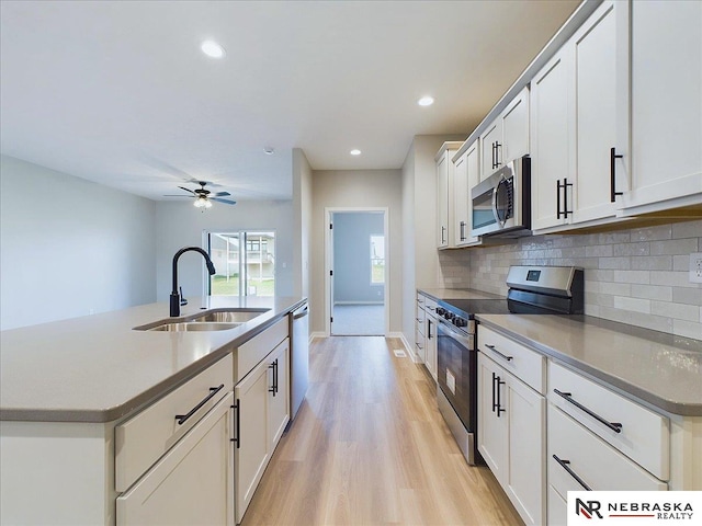 kitchen with appliances with stainless steel finishes, ceiling fan, sink, white cabinetry, and an island with sink