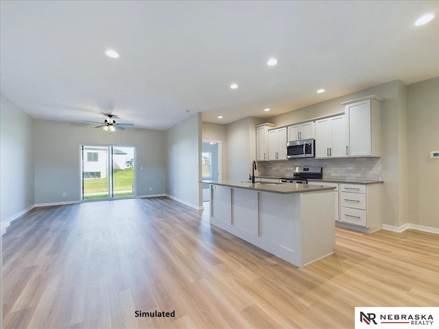 kitchen with light wood finished floors, tasteful backsplash, appliances with stainless steel finishes, a kitchen island with sink, and a sink