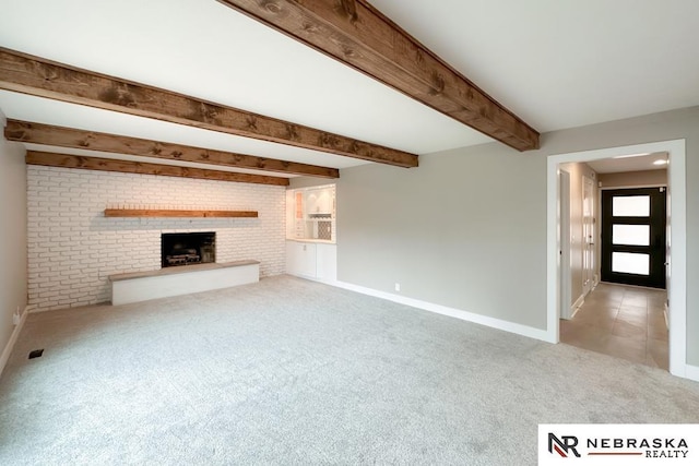 unfurnished living room with beam ceiling, light colored carpet, brick wall, and a brick fireplace