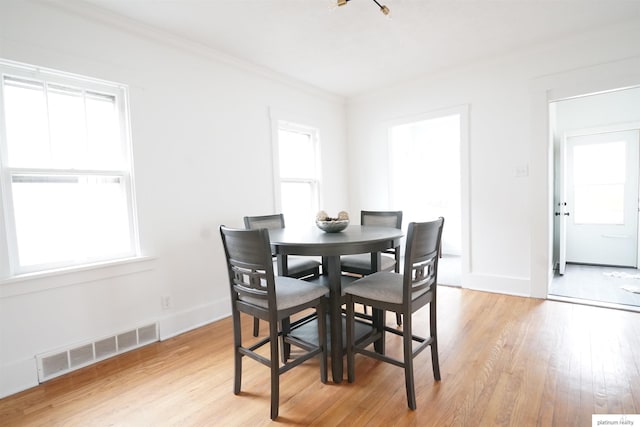 dining area featuring light wood-type flooring, crown molding, and a wealth of natural light