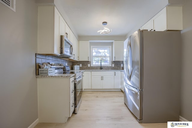 kitchen with white cabinets, sink, decorative backsplash, light stone countertops, and appliances with stainless steel finishes