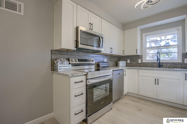 kitchen with sink, light stone counters, backsplash, white cabinets, and appliances with stainless steel finishes