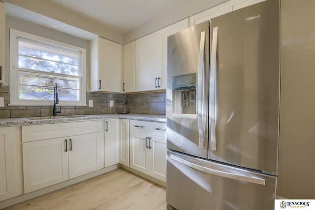 kitchen with light stone countertops, sink, backsplash, stainless steel fridge, and white cabinets