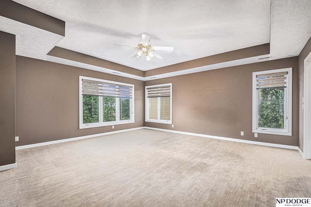 carpeted spare room with ceiling fan, a textured ceiling, and a tray ceiling