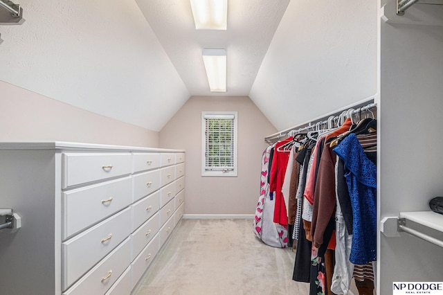 walk in closet with light colored carpet and vaulted ceiling