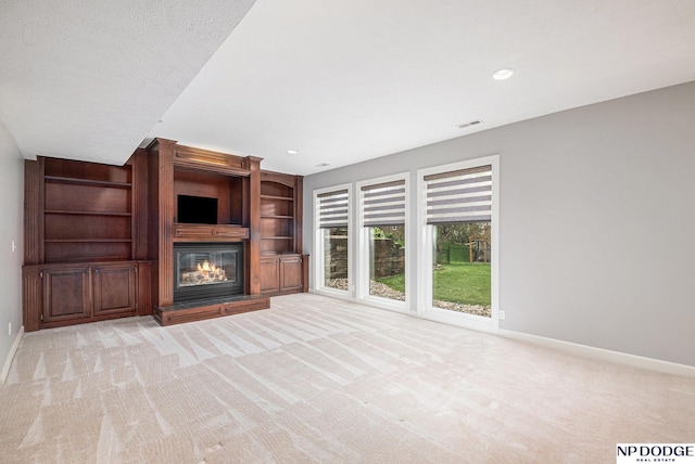 unfurnished living room with built in shelves, light colored carpet, and a textured ceiling