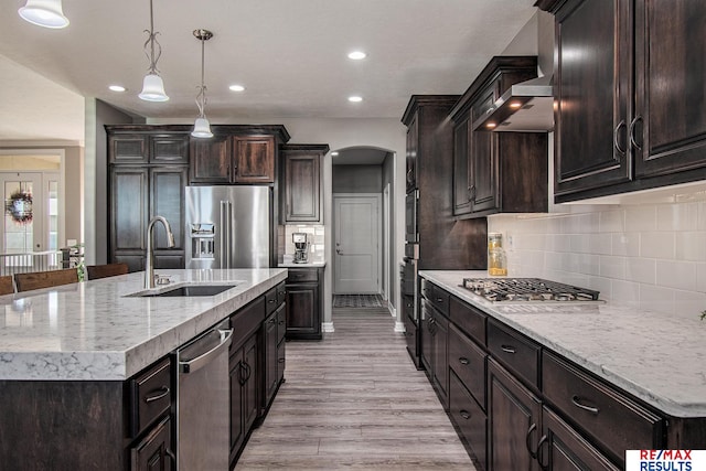 kitchen featuring sink, stainless steel appliances, light hardwood / wood-style flooring, an island with sink, and pendant lighting