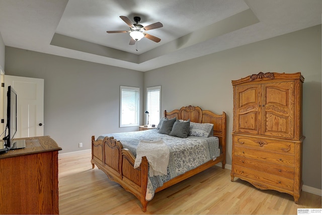 bedroom featuring a raised ceiling, ceiling fan, and light hardwood / wood-style flooring