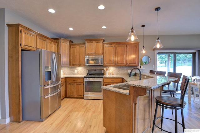 kitchen with brown cabinets, a peninsula, stainless steel appliances, and a sink