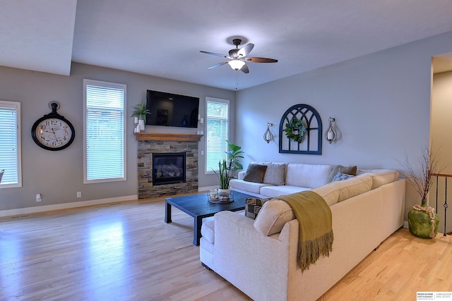 living room featuring baseboards, a stone fireplace, a ceiling fan, and light wood finished floors