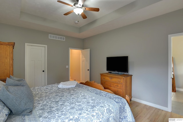 bedroom with a tray ceiling, ceiling fan, and light hardwood / wood-style flooring