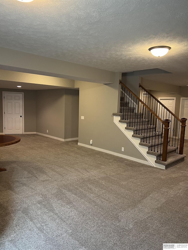 finished below grade area featuring stairway, carpet flooring, baseboards, and a textured ceiling