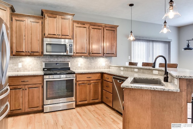 kitchen featuring sink, hanging light fixtures, light hardwood / wood-style flooring, appliances with stainless steel finishes, and light stone counters