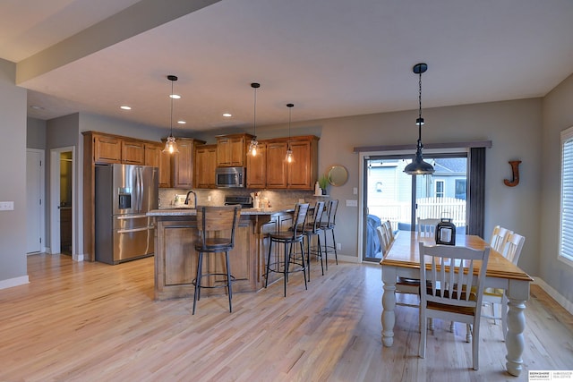 kitchen featuring tasteful backsplash, light stone counters, pendant lighting, appliances with stainless steel finishes, and light wood-type flooring