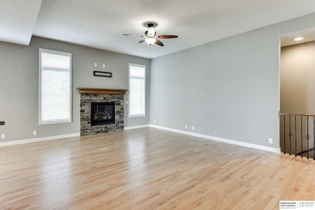 unfurnished living room with a stone fireplace, a ceiling fan, baseboards, and wood finished floors