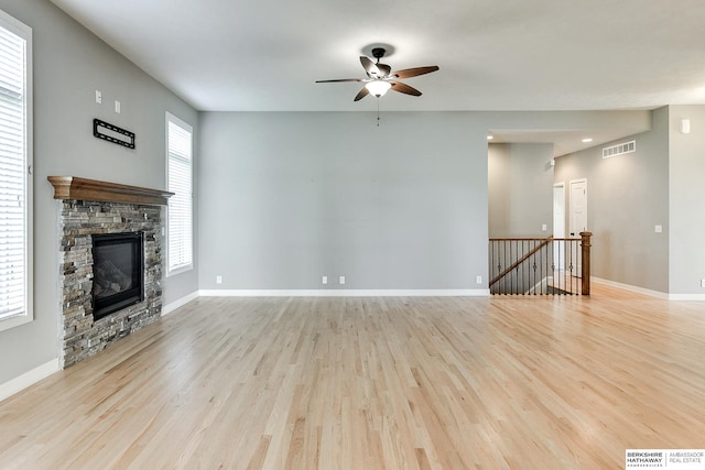 unfurnished living room with a stone fireplace, a wealth of natural light, and light hardwood / wood-style flooring