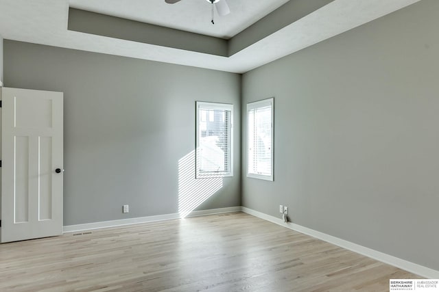 unfurnished room with a tray ceiling, light wood-style flooring, a ceiling fan, and baseboards