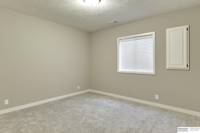 carpeted spare room with visible vents, a textured ceiling, and baseboards