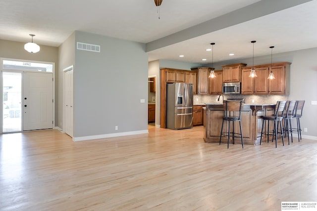 kitchen with appliances with stainless steel finishes, light hardwood / wood-style flooring, a center island, hanging light fixtures, and a breakfast bar area