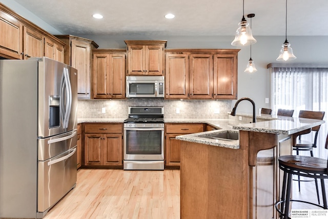 kitchen with a breakfast bar, sink, light stone countertops, kitchen peninsula, and stainless steel appliances