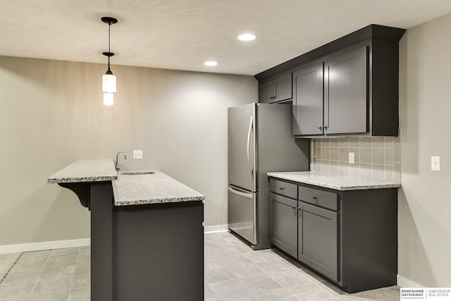 kitchen featuring a breakfast bar, a sink, tasteful backsplash, a peninsula, and light stone countertops