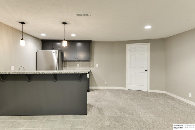 kitchen featuring visible vents, freestanding refrigerator, decorative backsplash, a kitchen bar, and light colored carpet