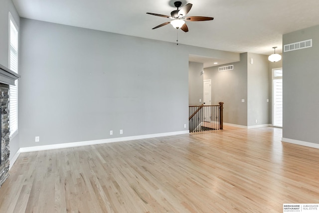 unfurnished living room with light hardwood / wood-style flooring, a stone fireplace, and ceiling fan