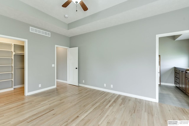 unfurnished bedroom featuring ceiling fan, a spacious closet, light hardwood / wood-style flooring, and a closet