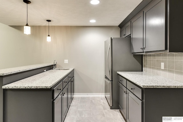 kitchen featuring a sink, backsplash, freestanding refrigerator, a peninsula, and baseboards