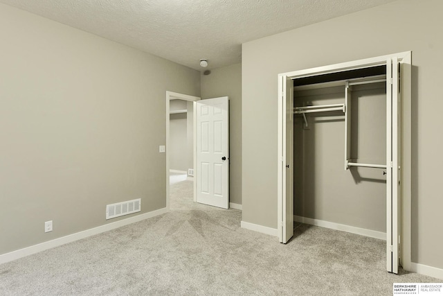 unfurnished bedroom with visible vents, a textured ceiling, a closet, baseboards, and light colored carpet