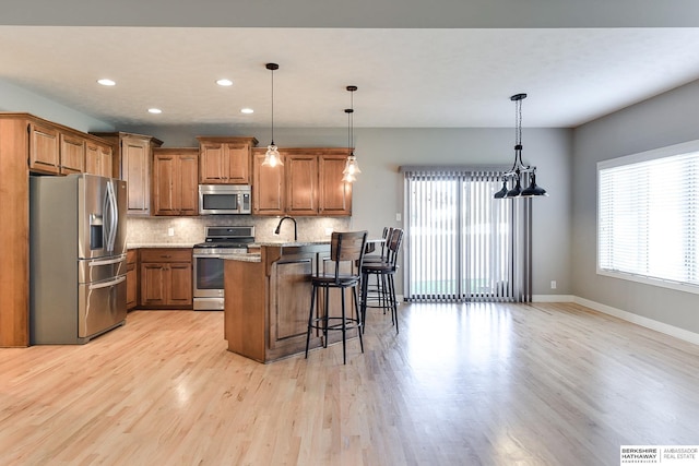 kitchen featuring pendant lighting, a kitchen breakfast bar, light wood-type flooring, light stone countertops, and appliances with stainless steel finishes