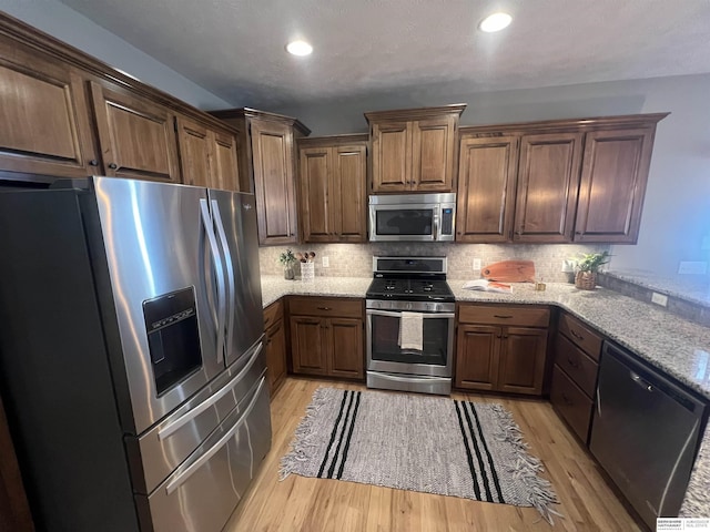 kitchen featuring light stone countertops, light wood-type flooring, decorative backsplash, recessed lighting, and appliances with stainless steel finishes