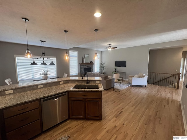 kitchen with light stone countertops, light wood-style flooring, a fireplace, stainless steel dishwasher, and a sink