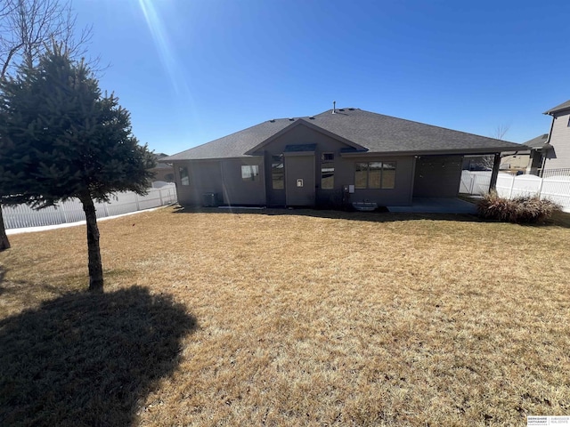 rear view of house with a patio area, a lawn, fence, and roof with shingles