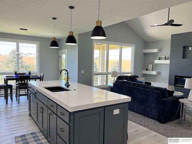 kitchen with sink, gray cabinetry, decorative light fixtures, light stone countertops, and a kitchen island with sink