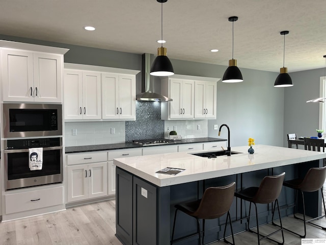 kitchen with decorative light fixtures, sink, white cabinets, a kitchen island with sink, and stainless steel appliances