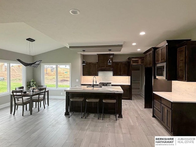 kitchen featuring stainless steel microwave, decorative light fixtures, sink, dark brown cabinetry, and a center island with sink