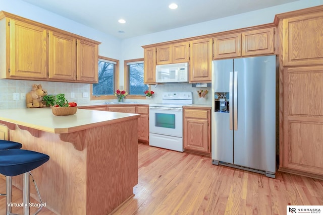 kitchen featuring a breakfast bar, white appliances, backsplash, light hardwood / wood-style flooring, and kitchen peninsula