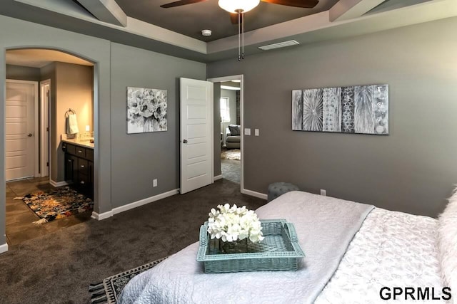 carpeted bedroom featuring ceiling fan, ensuite bath, and a tray ceiling