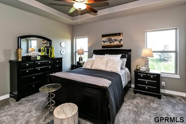 carpeted bedroom with ceiling fan and a tray ceiling