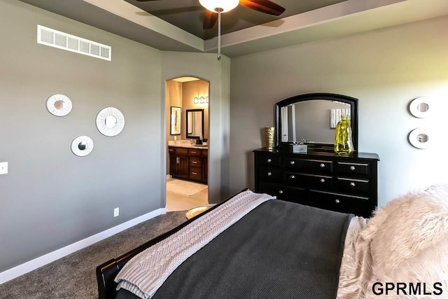 bedroom with ensuite bathroom, a raised ceiling, ceiling fan, and light carpet