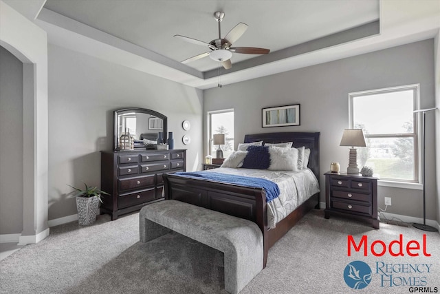 carpeted bedroom with ceiling fan and a tray ceiling