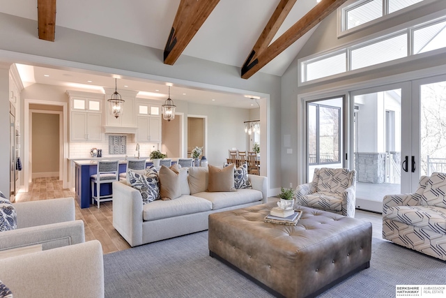 living room with french doors, sink, light wood-type flooring, beam ceiling, and a chandelier