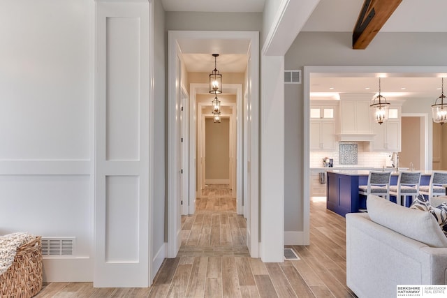 hall featuring beamed ceiling, sink, and light hardwood / wood-style flooring