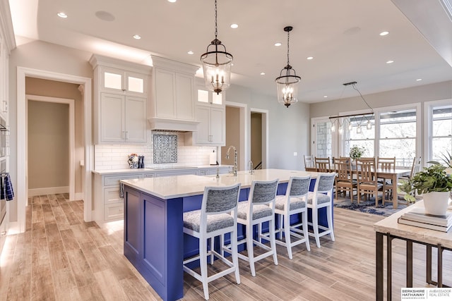 kitchen featuring light wood-type flooring, a kitchen island with sink, pendant lighting, a chandelier, and white cabinetry