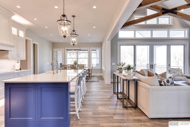 kitchen with backsplash, pendant lighting, a center island with sink, an inviting chandelier, and white cabinetry