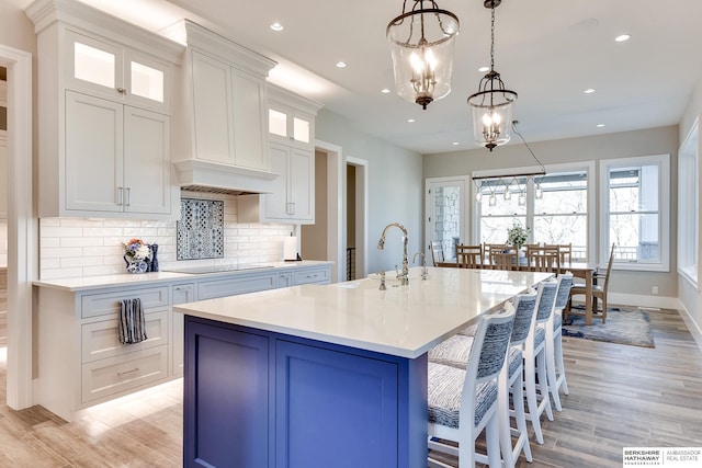 kitchen featuring a kitchen island with sink, sink, hanging light fixtures, white cabinetry, and a chandelier