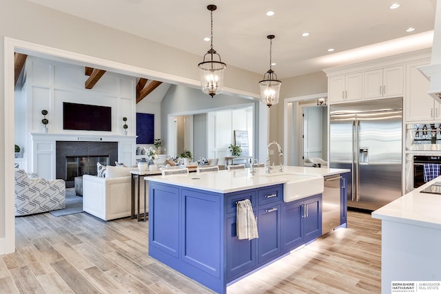 kitchen featuring appliances with stainless steel finishes, blue cabinetry, decorative light fixtures, white cabinetry, and an island with sink